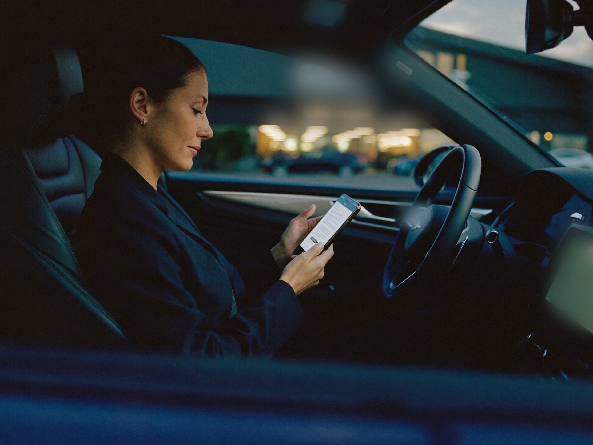 A buyer reading a reply on her phone in her car in the evening