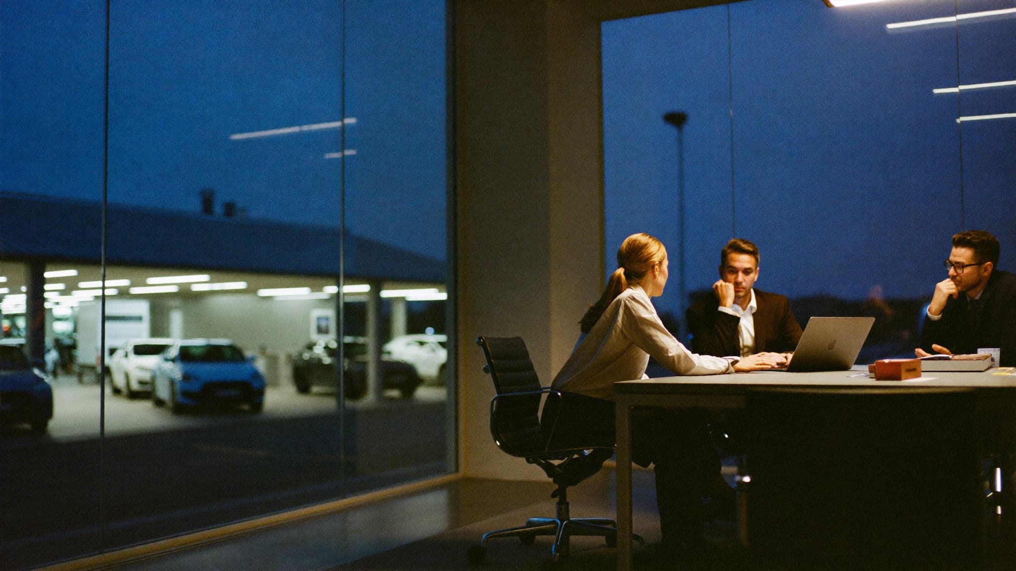 A dealership team reviewing a laptop in a meeting room above the showroom